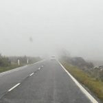 Car driving carefully through fog on a Spanish road.