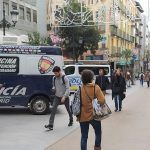 Pedestrians crossing a busy street near shops or a leisure area.